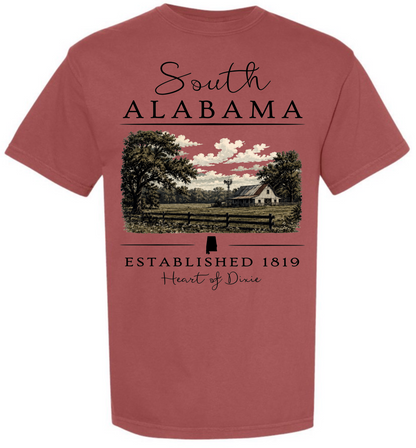 A dusty rose short-sleeve t-shirt with a graphic print on the front. The graphic features the text 'South ALABAMA' in black script and block lettering above a scenic landscape illustration of a farm with trees, a fence, and a farmhouse under a cloudy sky.